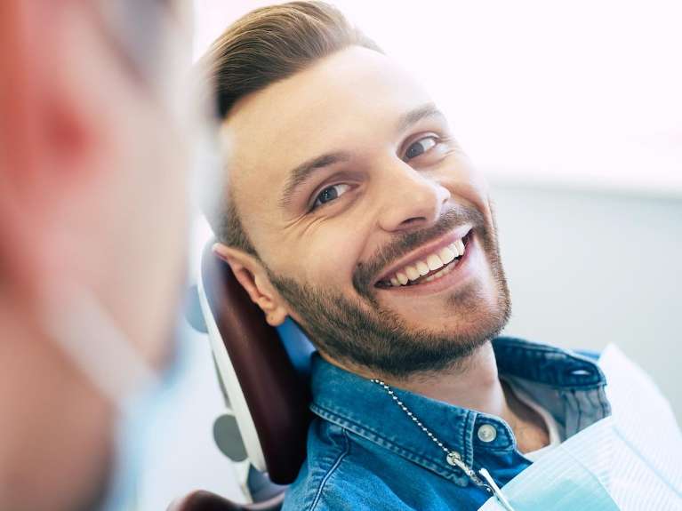 Smiling man sitting in a dental chair, wearing a protective bib.