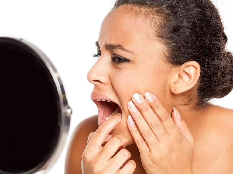 Woman looking into a mirror with a distressed expression.